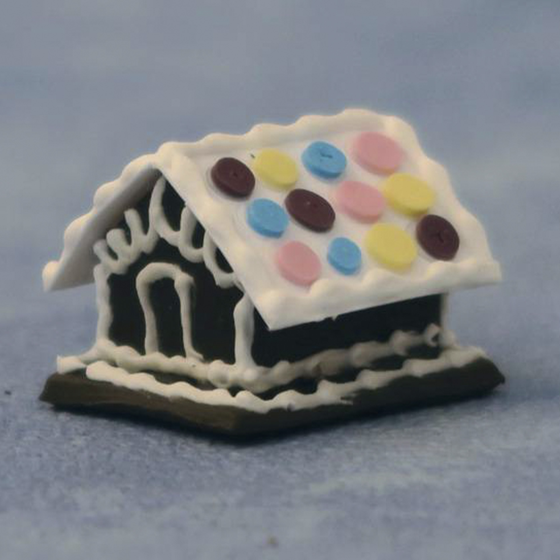 braunes Lebkuchenhaus mit weißer Verzierung und weißem Dach mit bunten Punkten